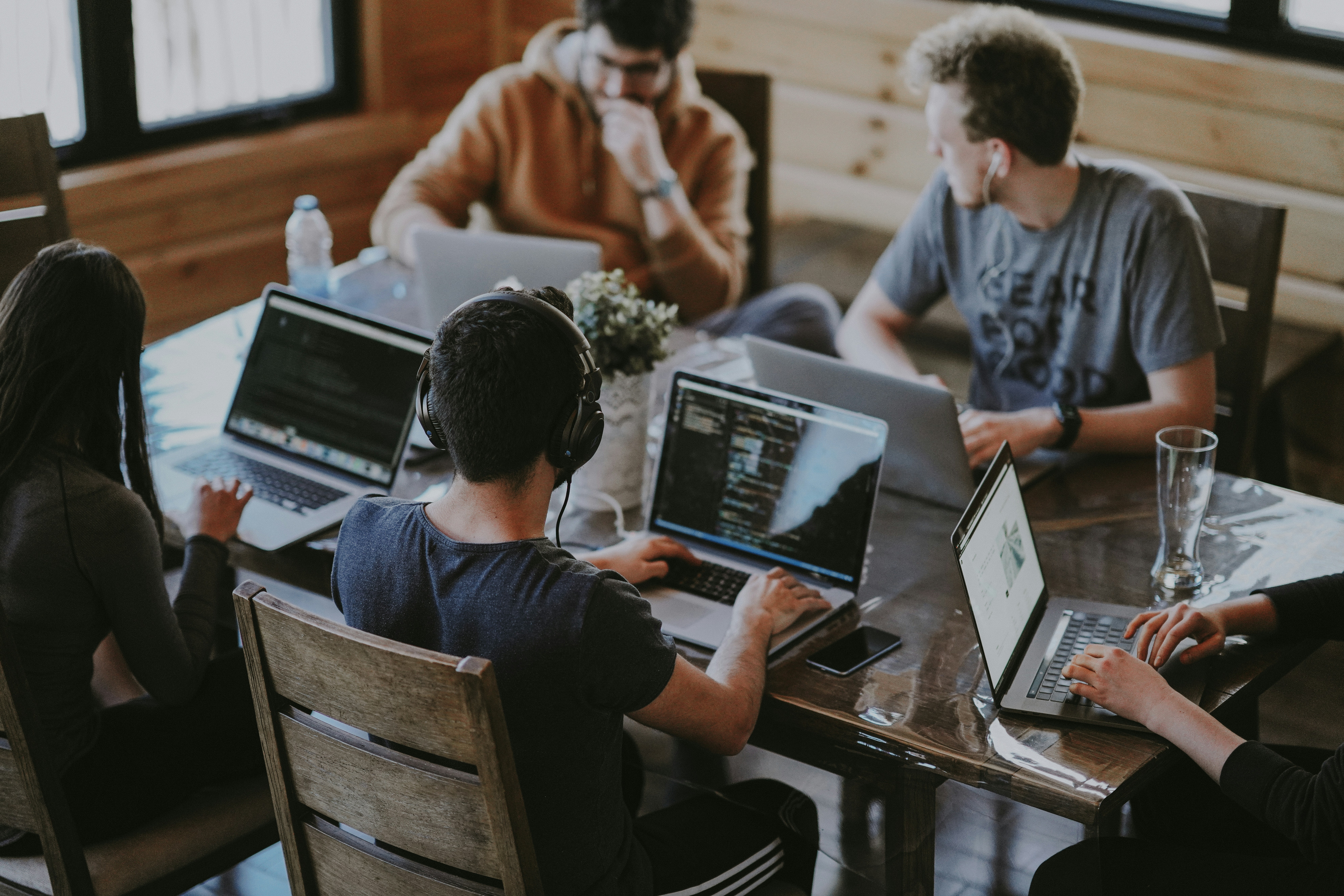 A group of 5 sitting at a table all collaborating on laptops.